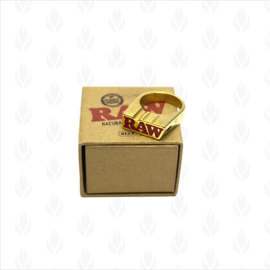 Anillo RAW dorado para fumar sobre caja de cartón marrón con el logotipo de RAW en la tapa